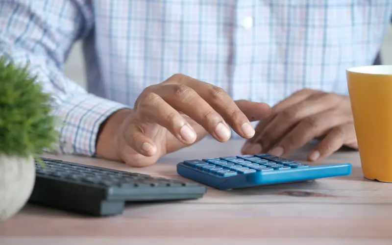 Person using a calculator beside a laptop at a desk